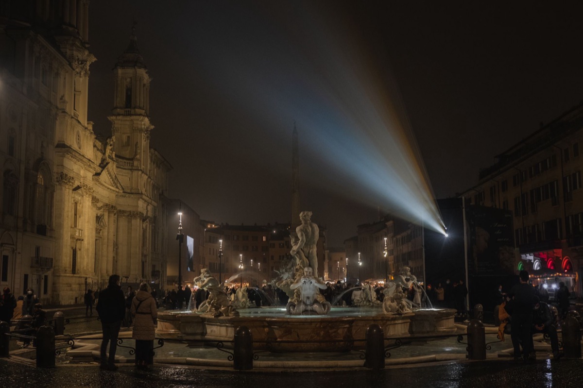 Tourists and locals at piazza with fountain and statue