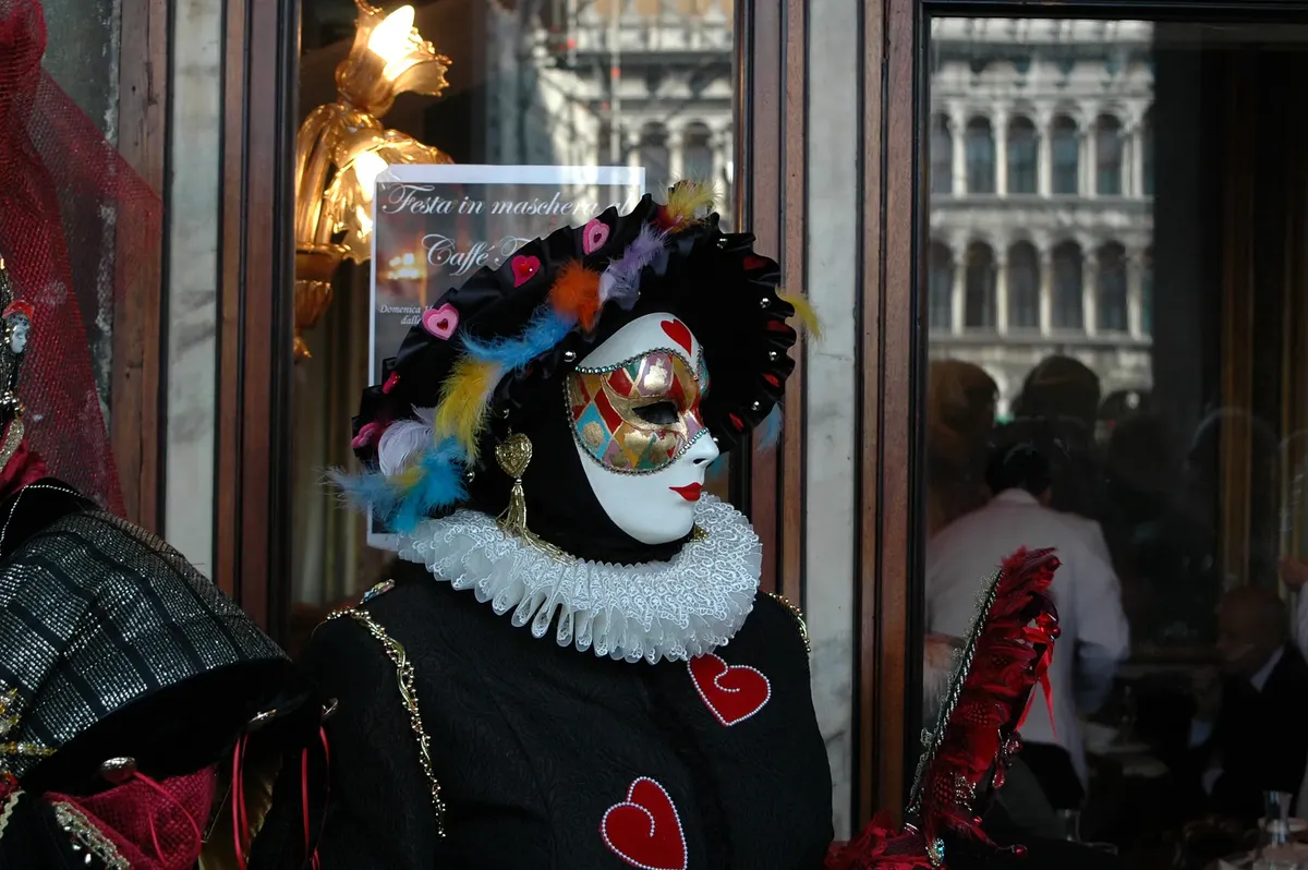 A colorful masked figure with heart motifs at a Venetian carnival, showcasing traditional attire.